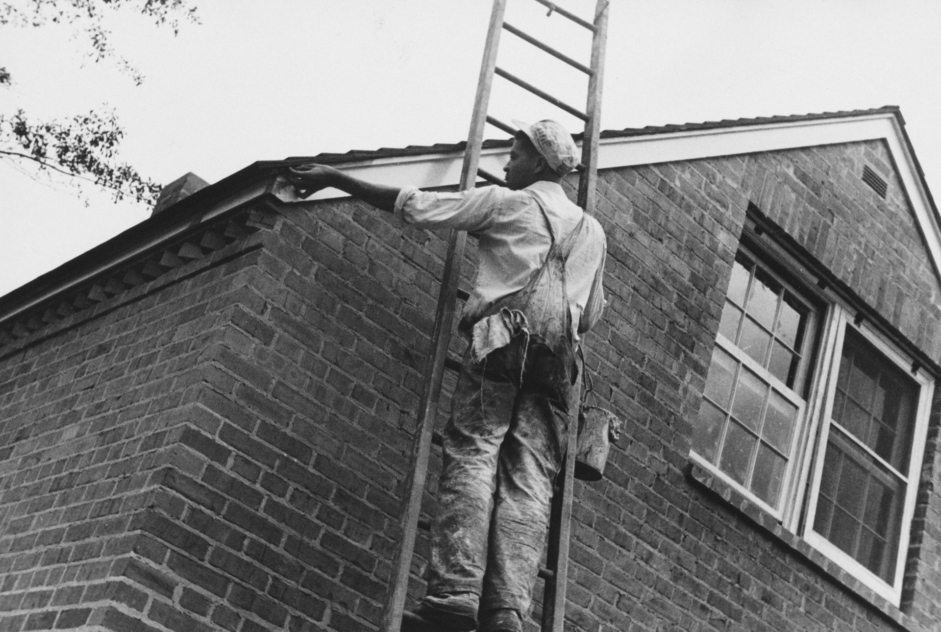 Amos on a ladder working on a brick home, late 1940s or early 1950s.